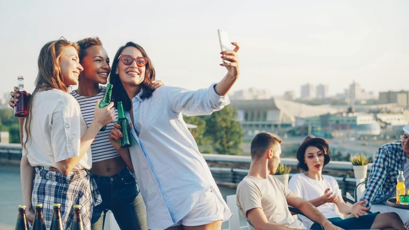 Three friends taking a selfie with a phone at a rooftop party